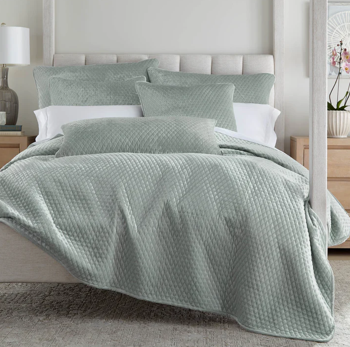 Soft green velvet coverlet with matching pillows on a layered bed